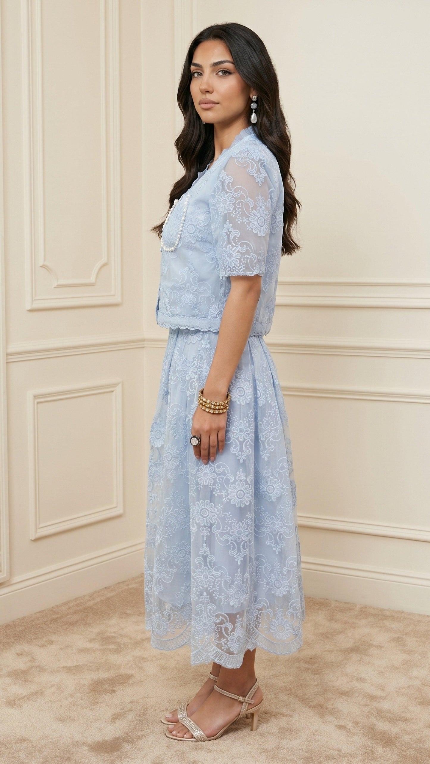Woman wearing a light blue lace dress against a beige wall.
