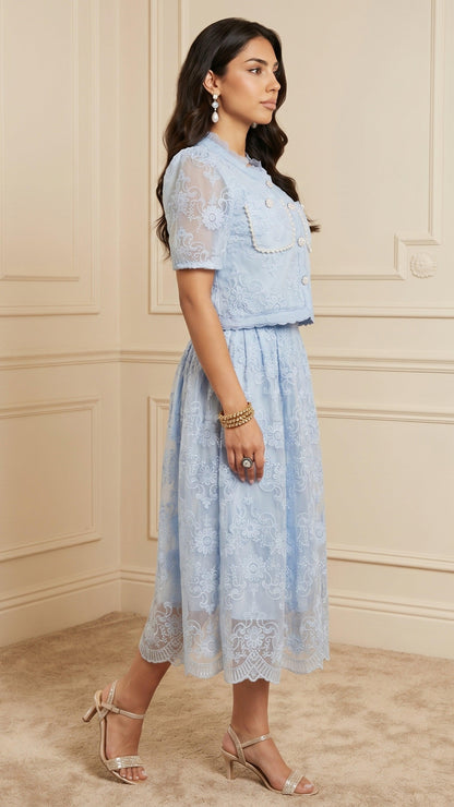 Woman wearing a light blue lace dress standing against a beige wall.