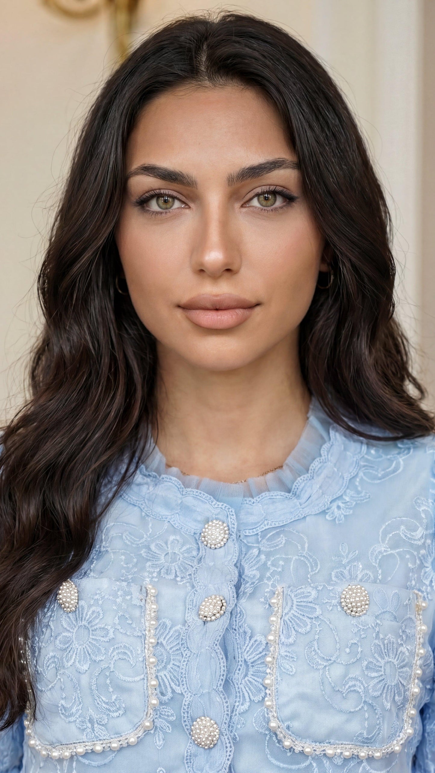 Woman wearing a light blue embroidered blouse with a neutral background