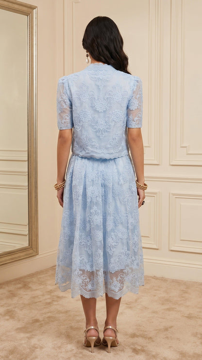 Woman wearing a light blue lace dress in a room with beige walls.