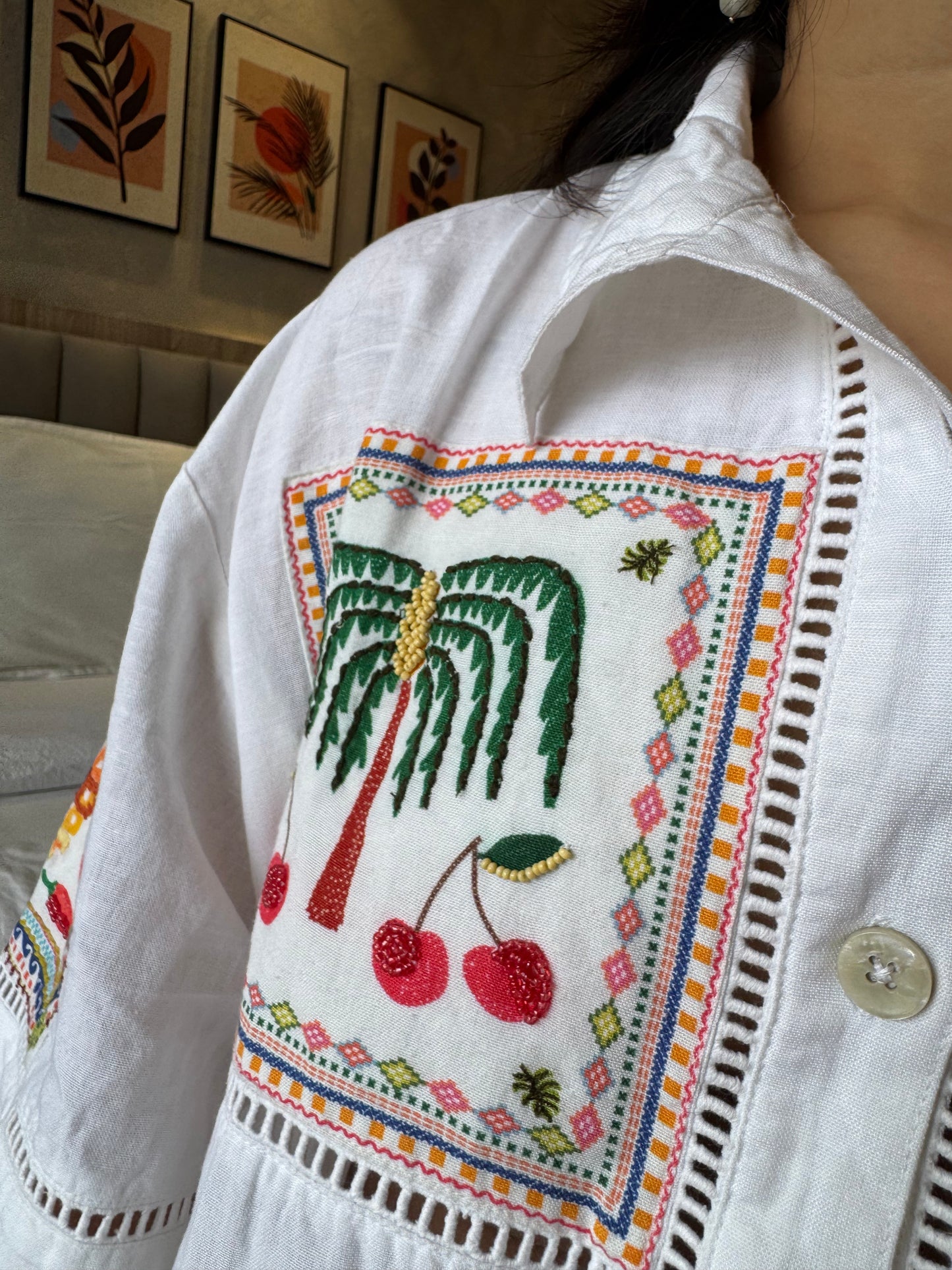 Close-up of a white embroidered shirt with palm tree and cherry design.