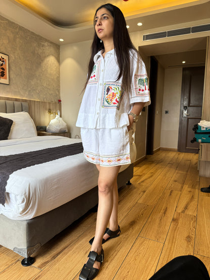 Woman in a white embroidered outfit standing in a bedroom.
