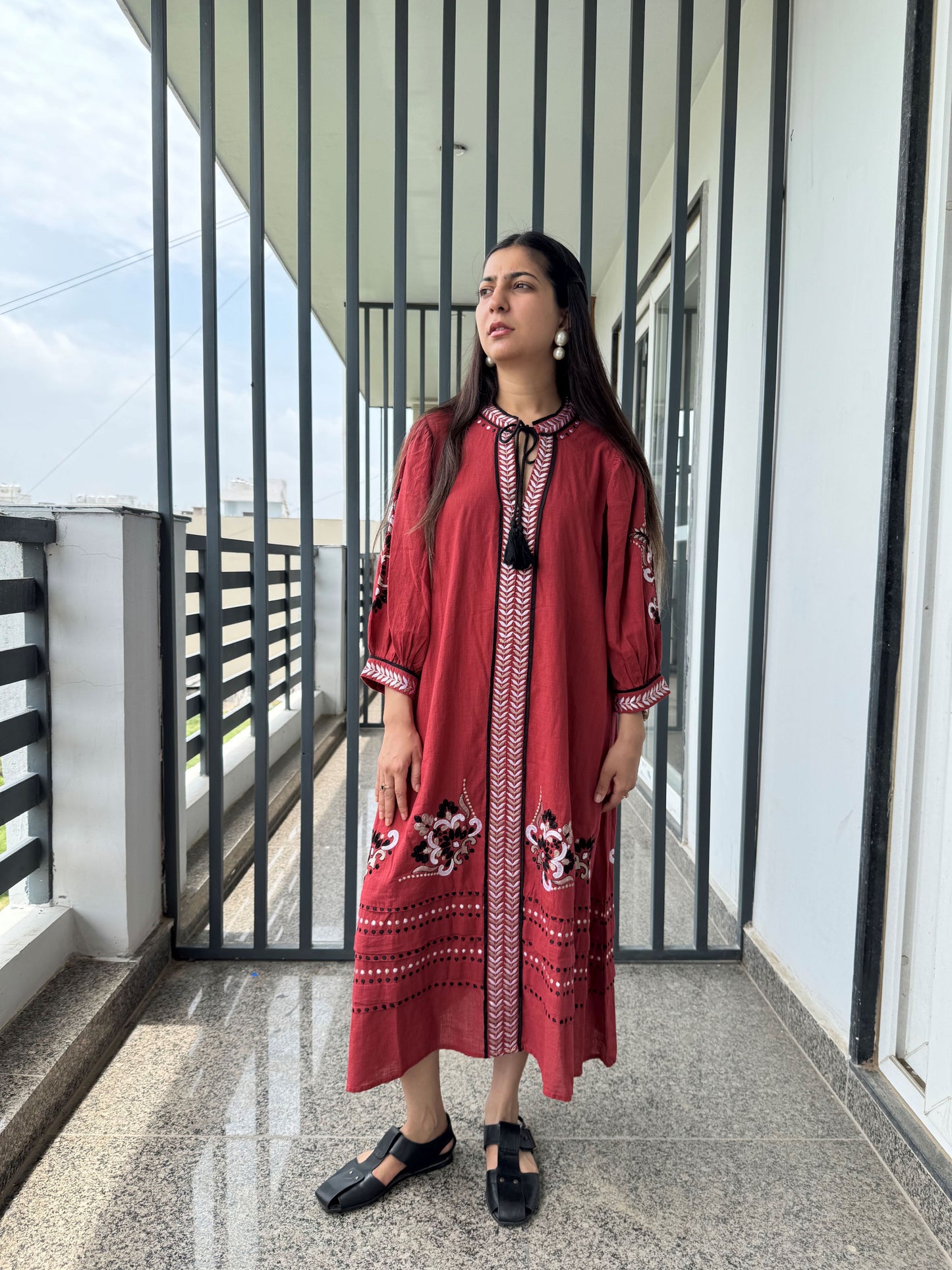 Woman in a red embroidered dress standing on a balcony
