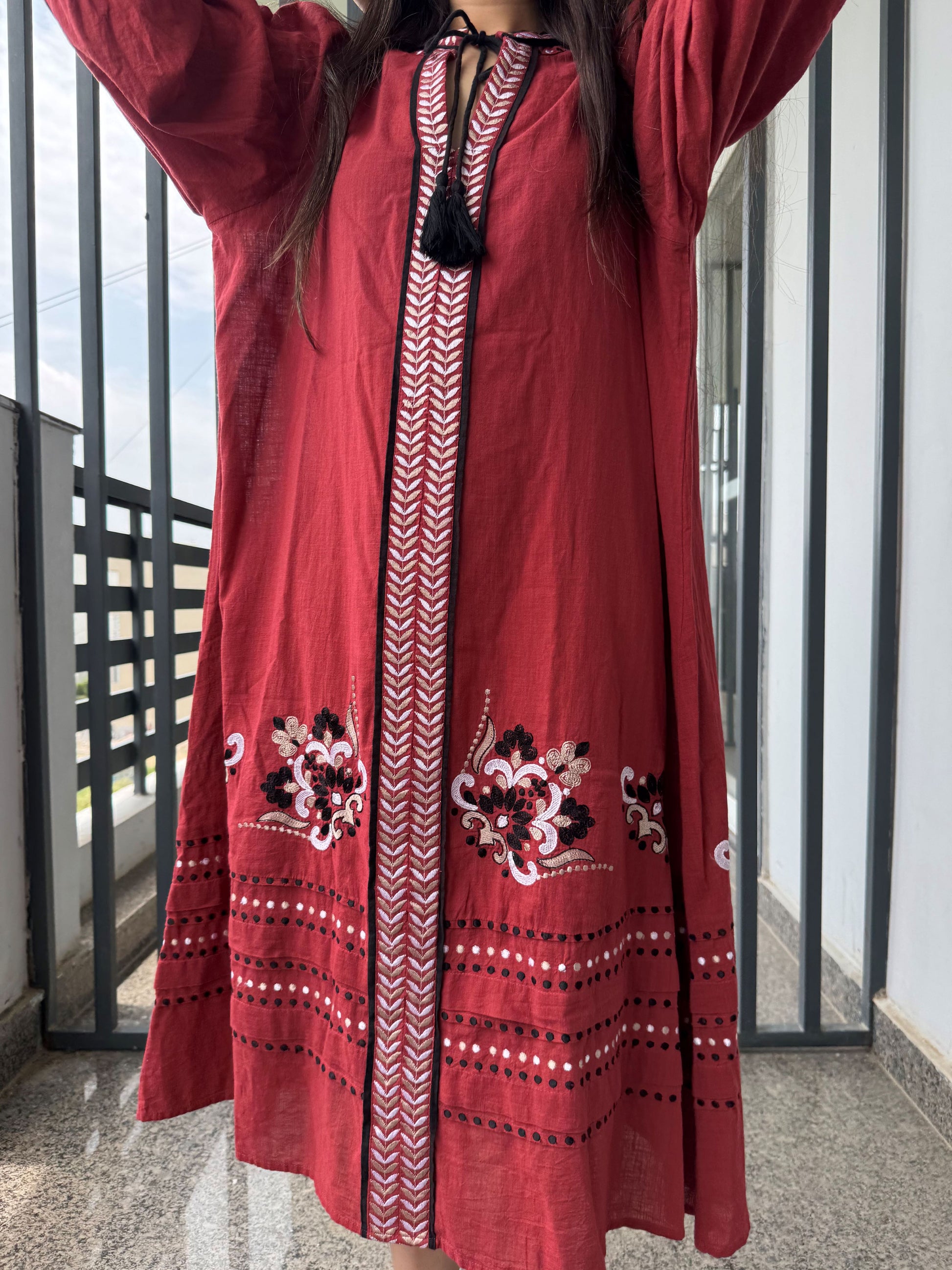 Red embroidered dress with intricate patterns worn by a person on a balcony.
