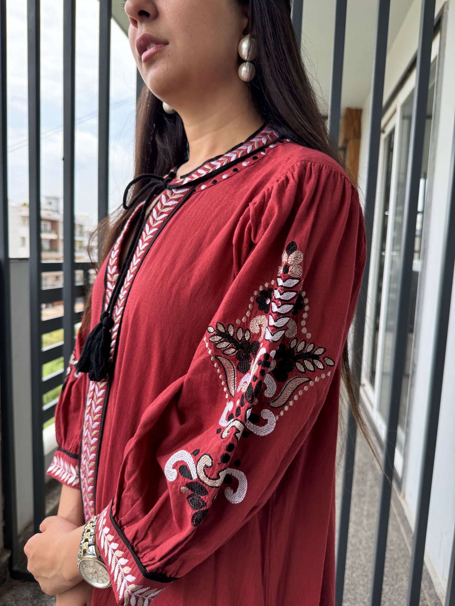 Woman wearing a red embroidered dress standing outdoors.