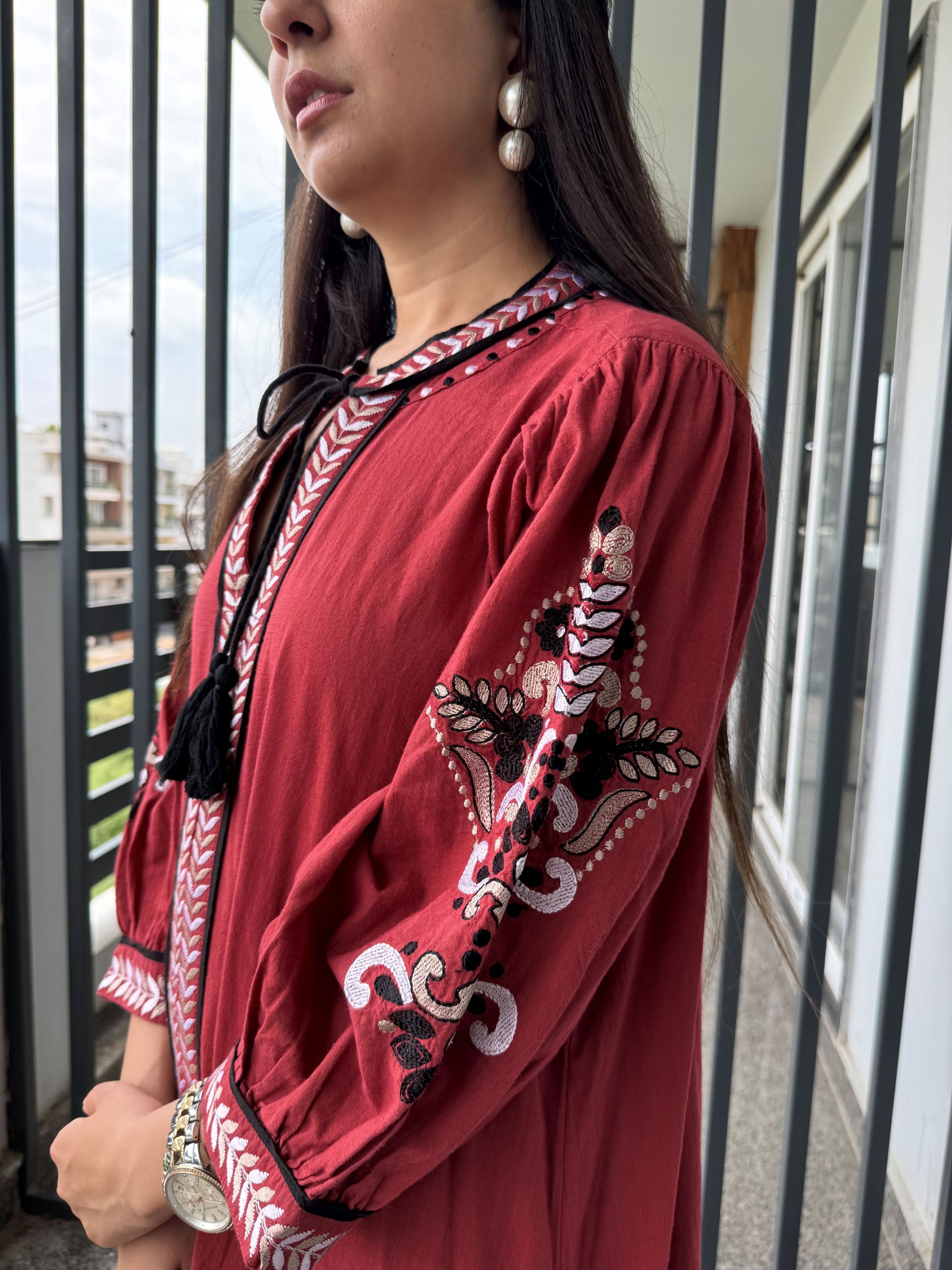 Woman wearing a red embroidered dress standing outdoors.