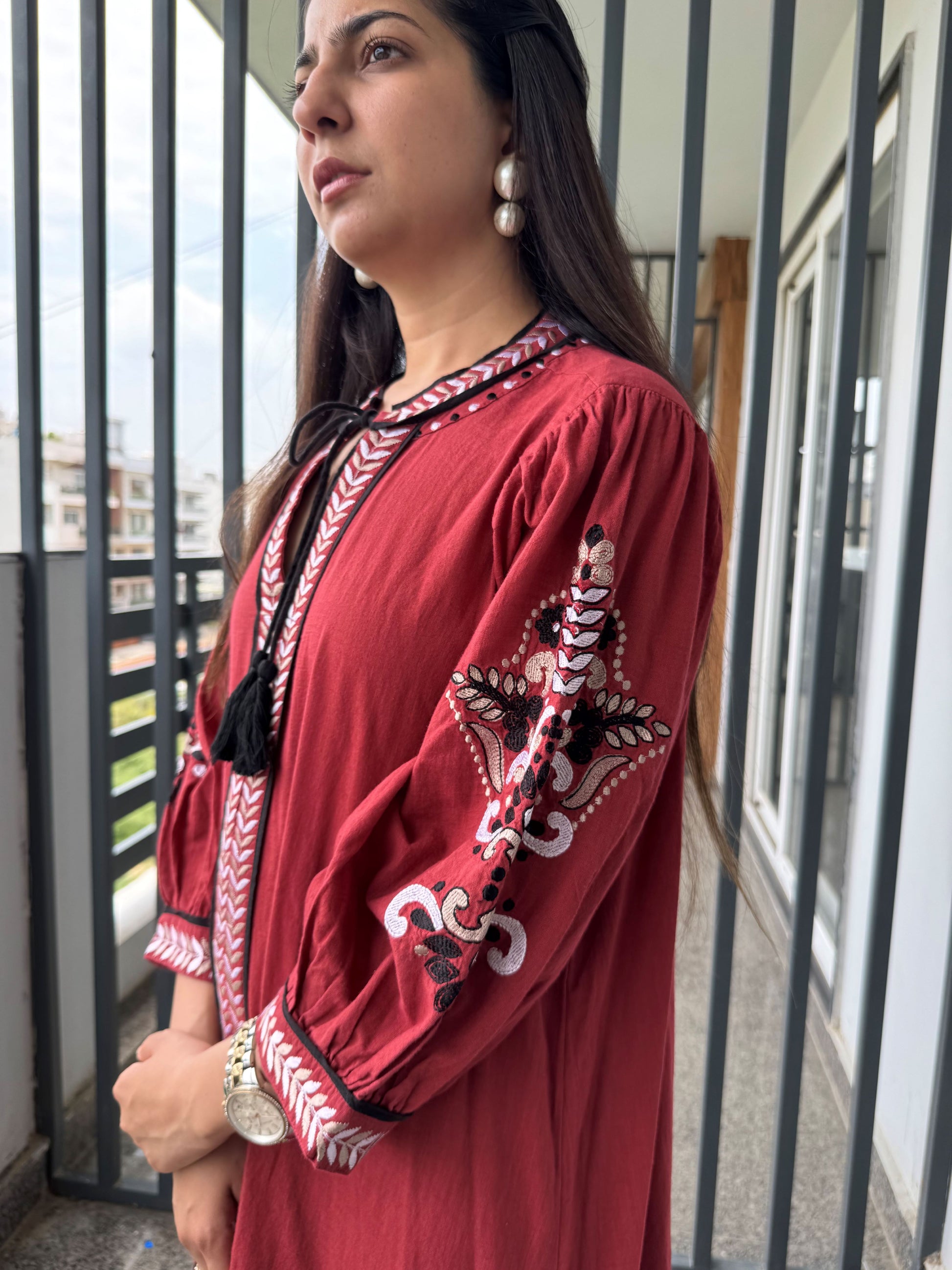 Woman wearing a red embroidered dress standing outdoors.