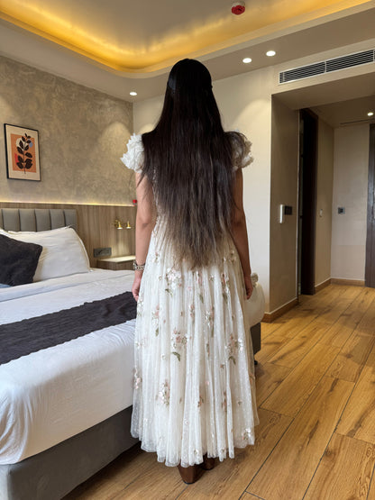 Woman in a white dress standing in a bedroom looking at a bed.