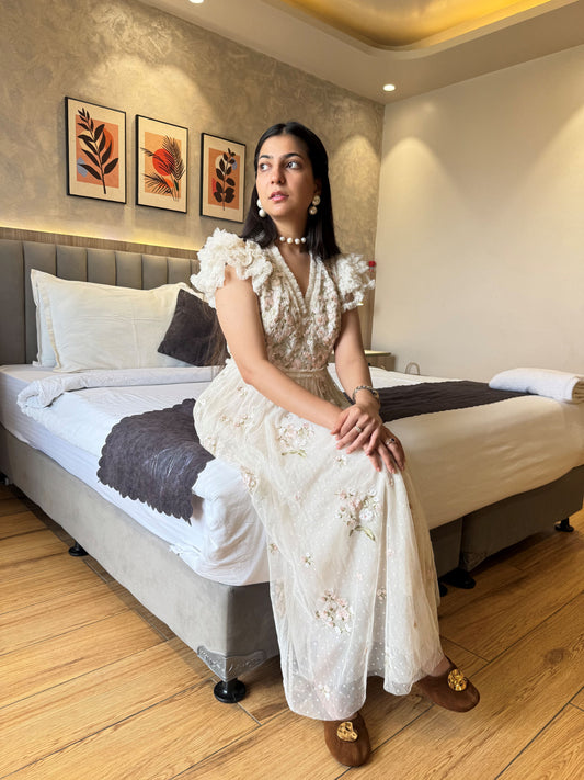 Woman in a white dress sitting on a bed in a stylish bedroom.
