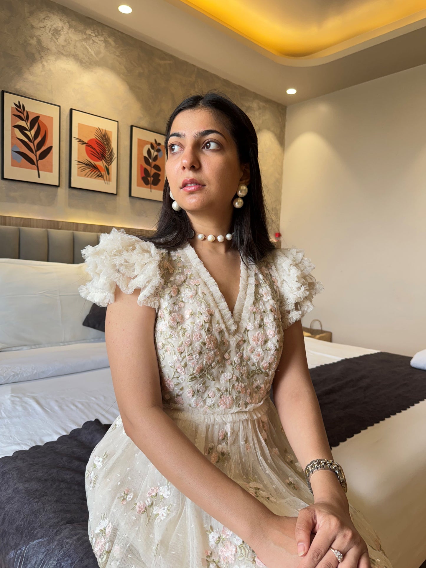 Woman in a white floral dress sitting on a bed in a decorated room.