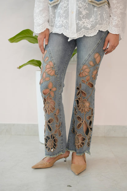 Person wearing floral embroidered jeans with a white lace top against a plain background