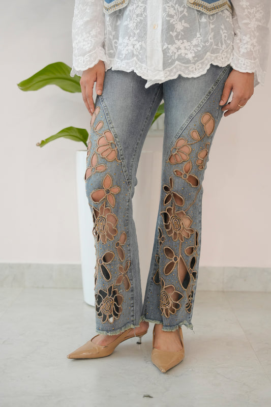Person wearing floral embroidered jeans with a white lace top against a plain background