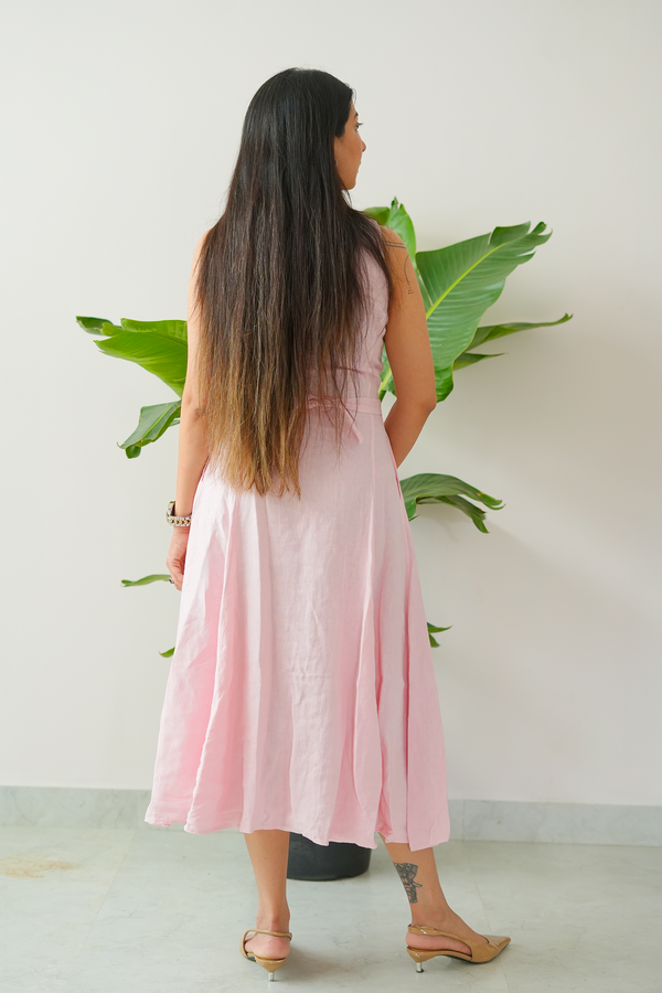 Woman in a pink dress standing in front of a white wall with a plant.