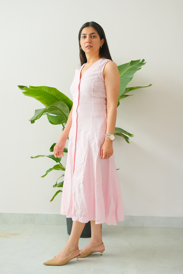 Woman wearing a light pink sleeveless dress with a white background and green plants.