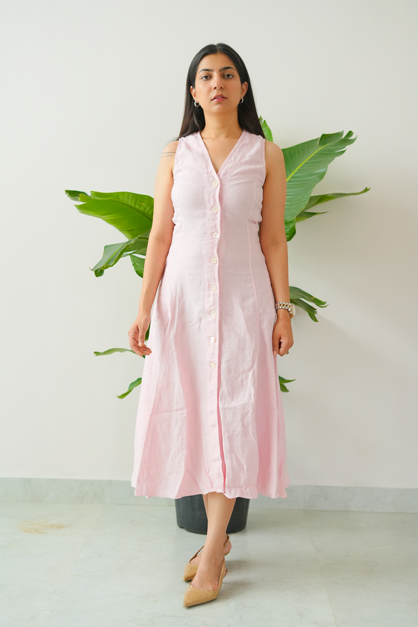 Woman wearing a light pink sleeveless dress standing against a white wall with green plants.
