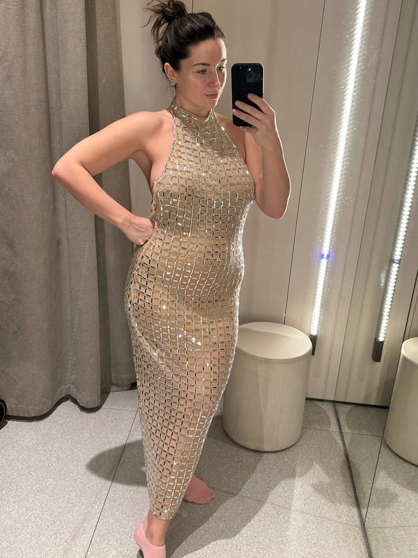 Woman taking a mirror selfie wearing a sparkly gold dress in a room with neutral decor.