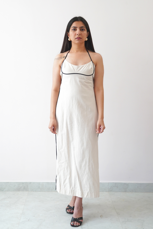 Woman wearing a white slip dress with black trim against a plain background