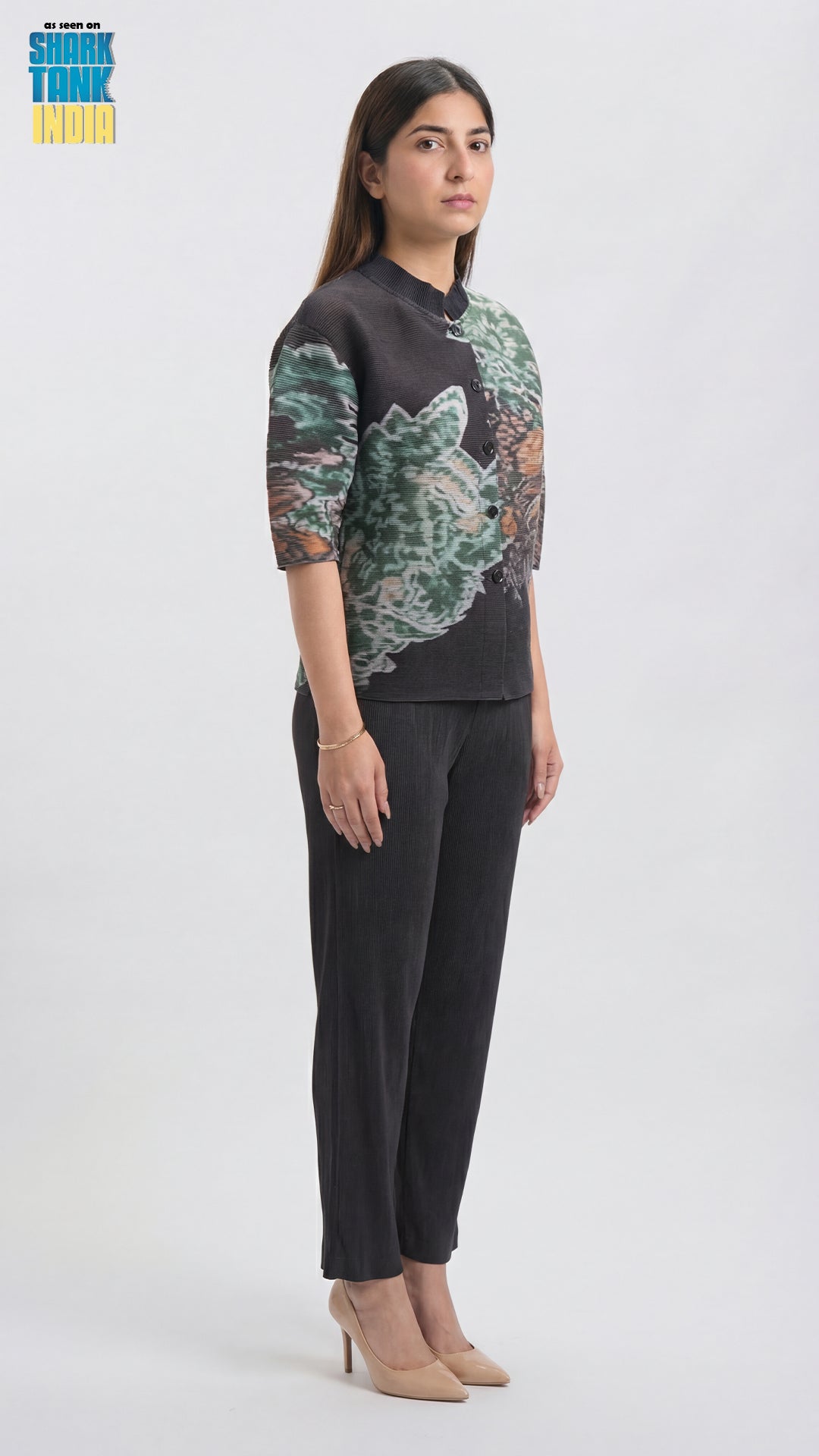 Woman wearing a patterned top and black pants on a white background