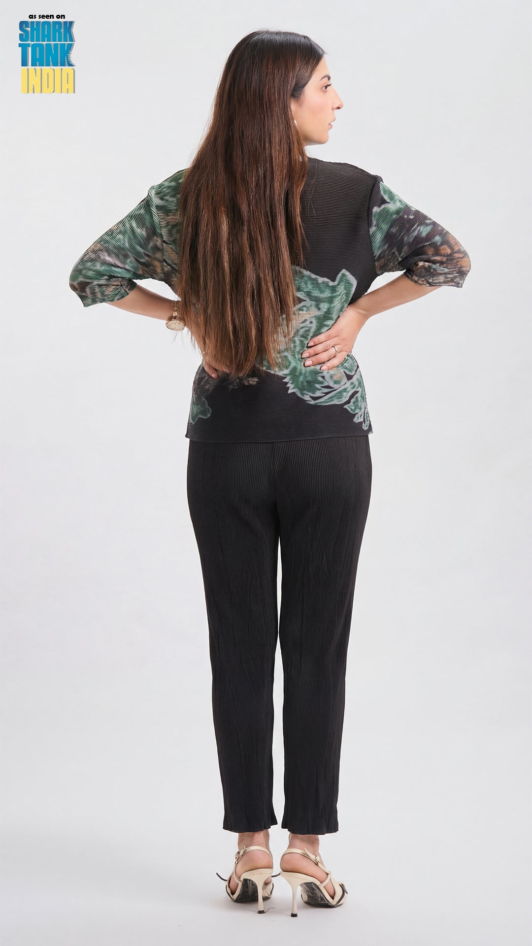 Woman wearing a green patterned top and black pants on a white background