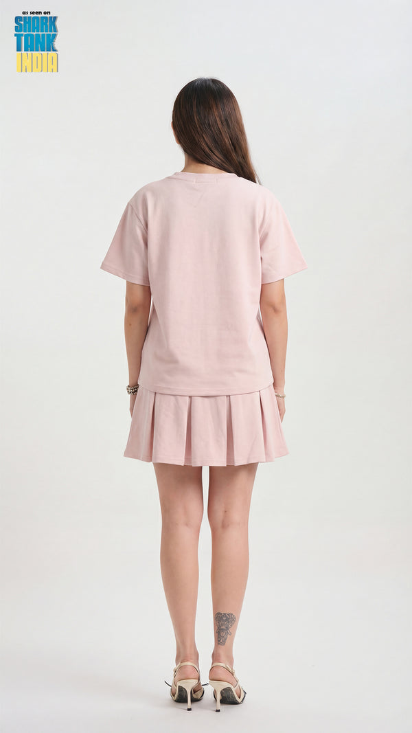 Person wearing a pink outfit with a pleated skirt on a white background
