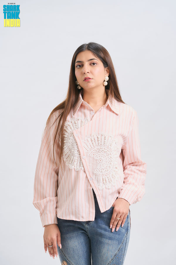 Woman wearing a light pink blouse with intricate patterns and blue jeans on a white background