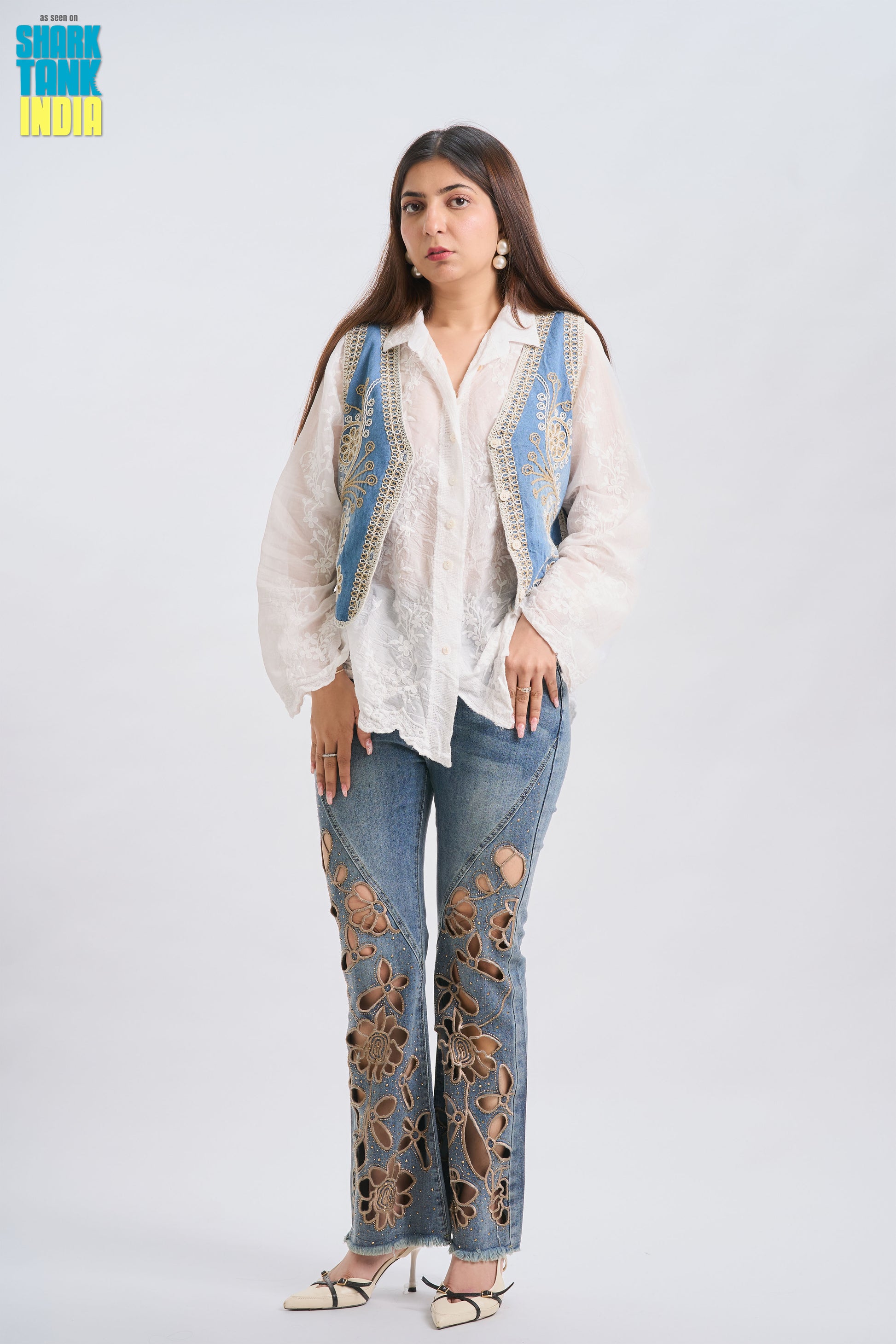 Woman wearing a white blouse with blue embroidery and floral-patterned jeans on a white background