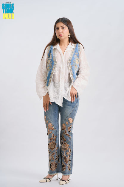 Woman wearing a white blouse with blue embroidery and floral-patterned jeans on a white background