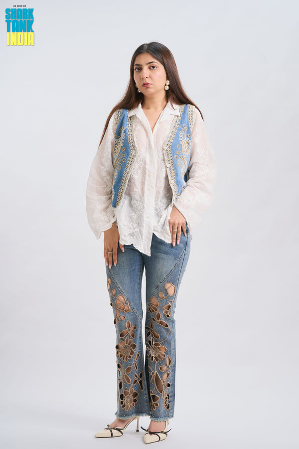 Woman wearing a white blouse with blue embroidery and floral-patterned jeans on a white background