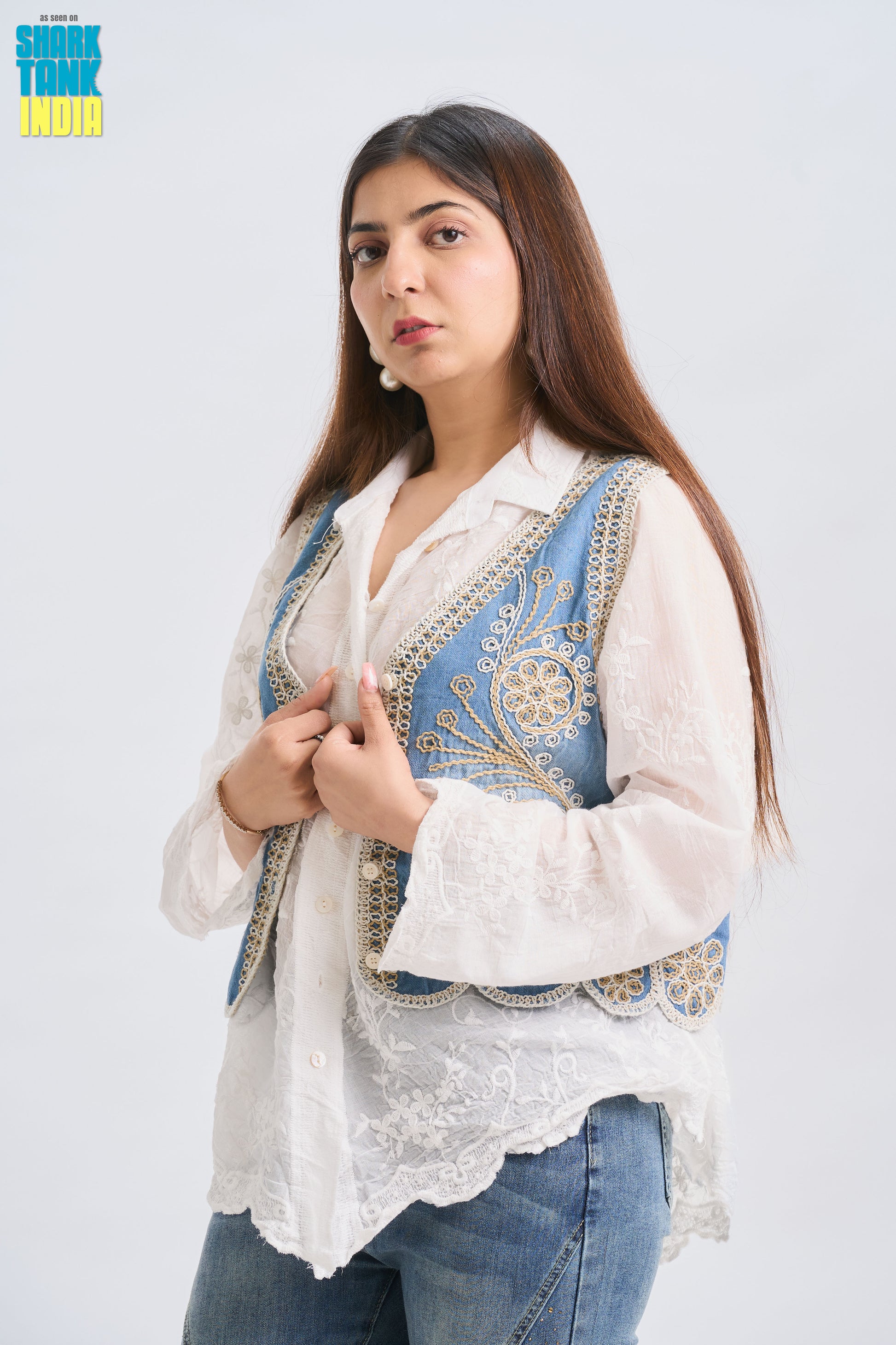 Woman wearing a white blouse with blue embroidery and jeans on a light gray background