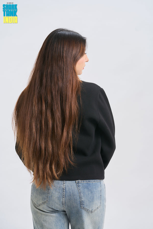 Person with long brown hair wearing a black sweater and blue jeans on a white background