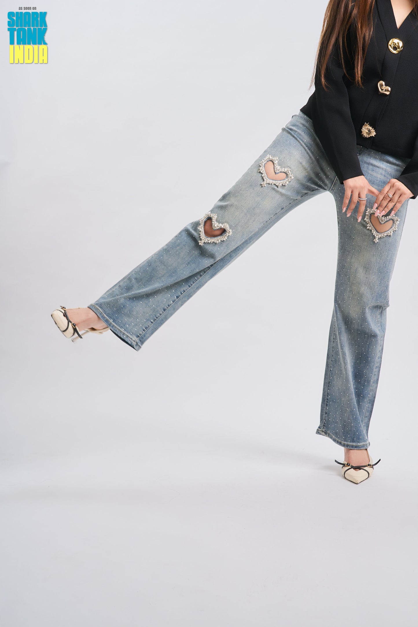 Person wearing a black top with gold buttons and ripped blue jeans on a white background