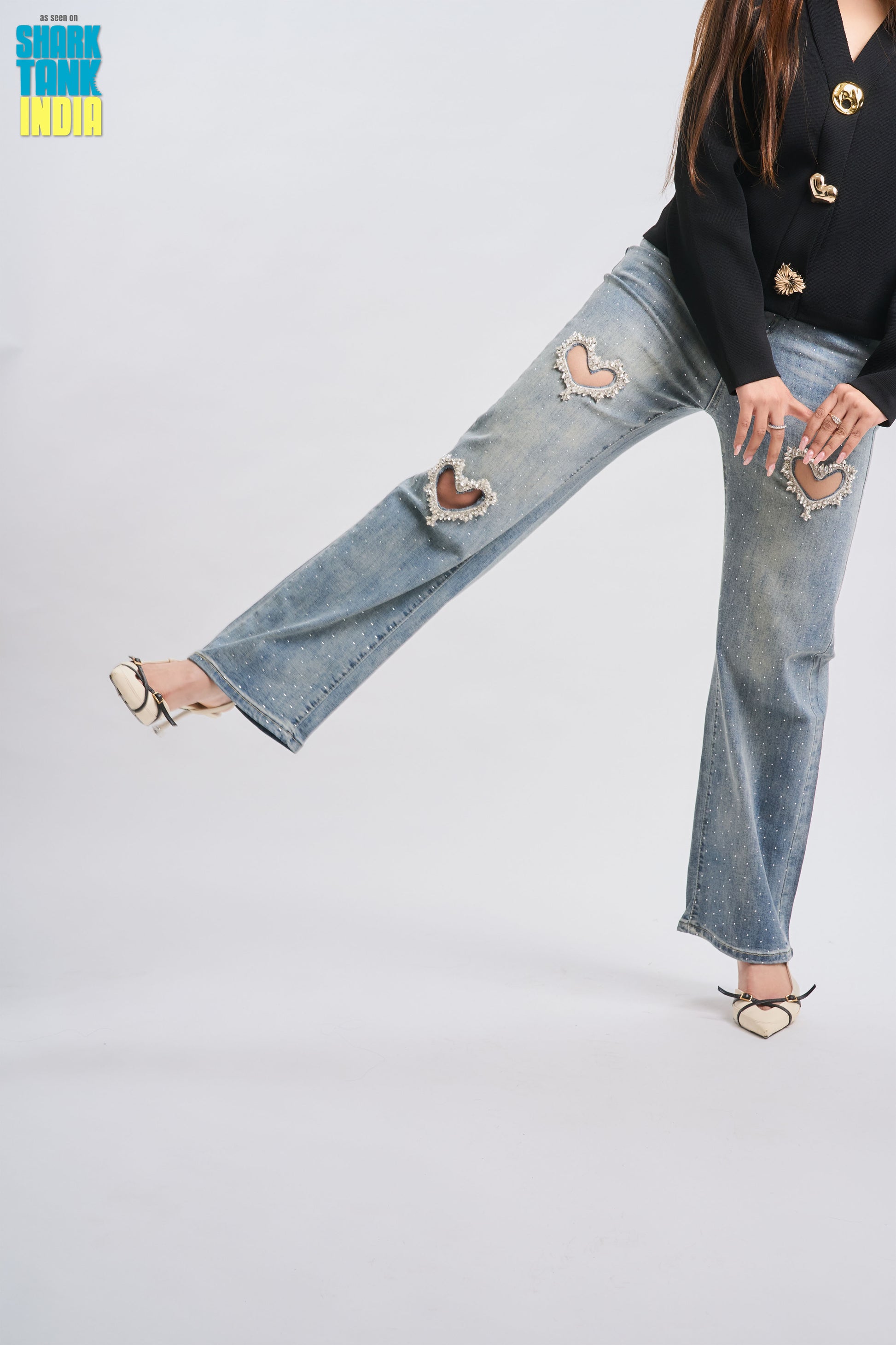 Person wearing a black top with gold buttons and ripped blue jeans on a white background