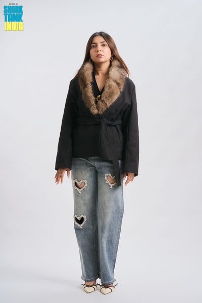 Woman wearing a black coat with fur collar and ripped jeans on a white background