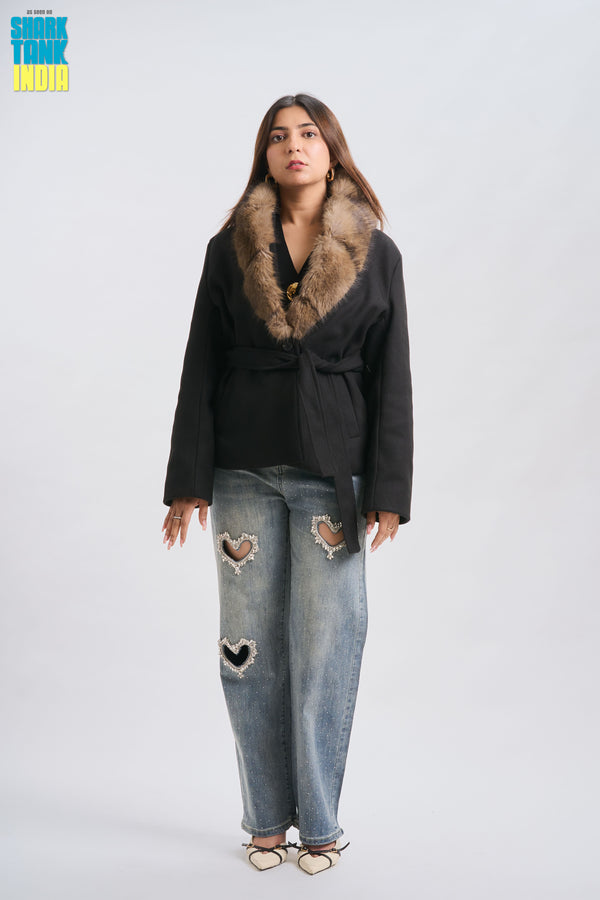 Woman wearing a black coat with fur collar and ripped jeans on a white background
