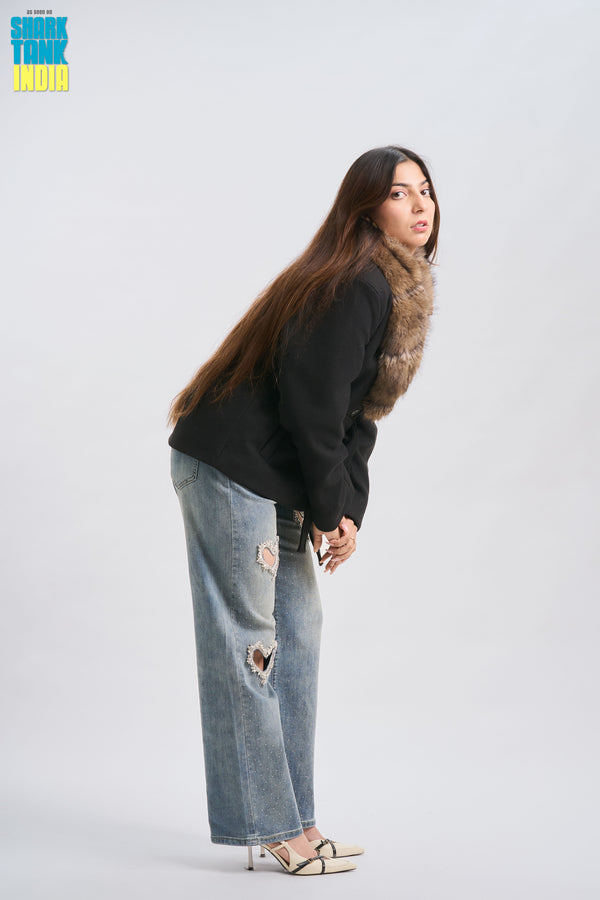 Woman wearing a black hoodie with fur trim and ripped jeans on a white background