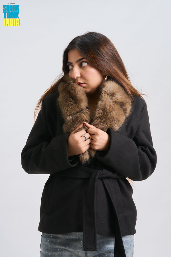 Woman wearing a black coat with a fur collar on a plain background