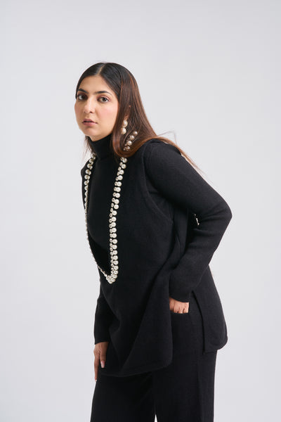 Woman wearing a black outfit with a long necklace on a white background