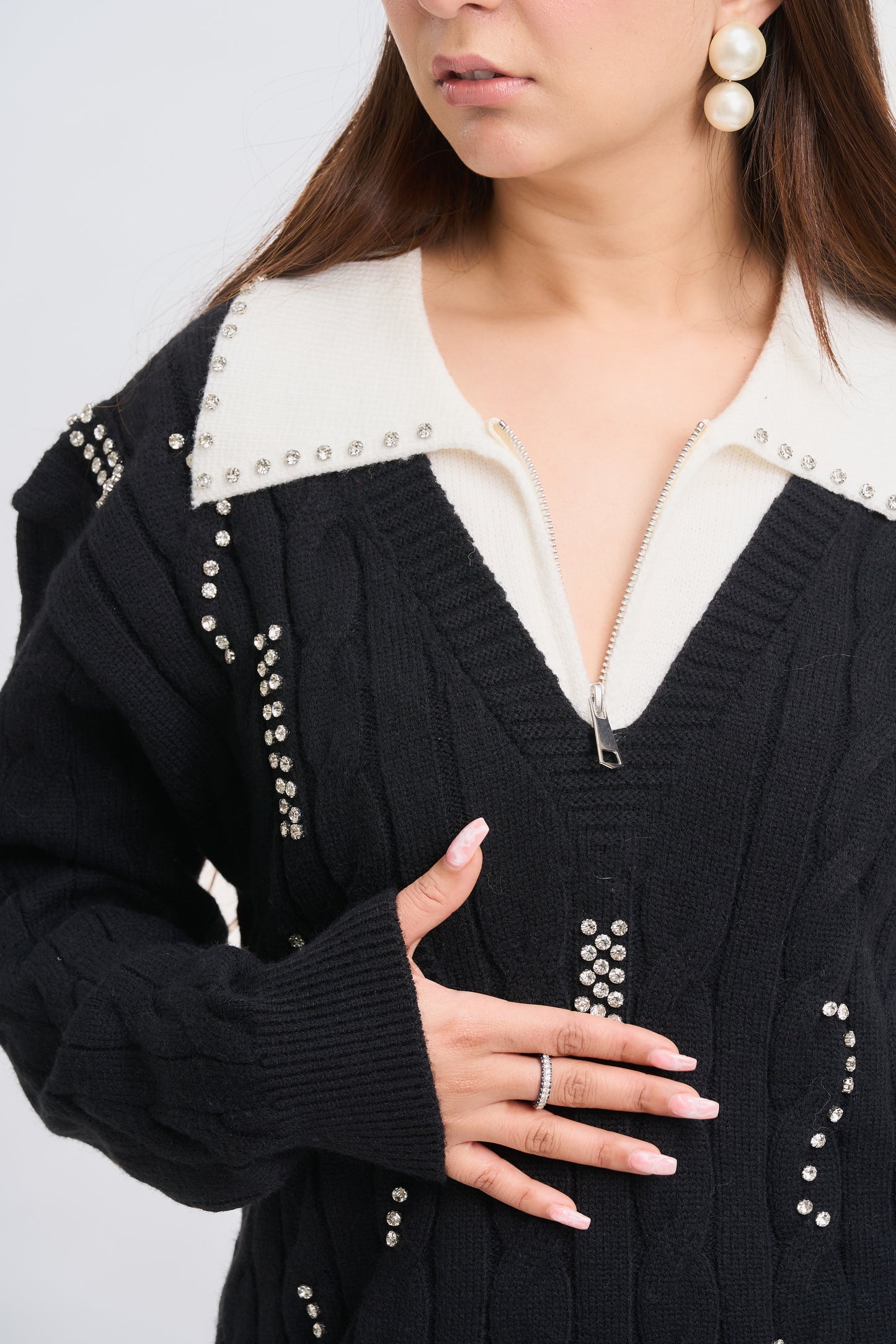 Person wearing a black cardigan with pearl embellishments on a light gray background