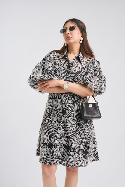 Woman wearing a black and white patterned dress with sunglasses and a handbag on a white background