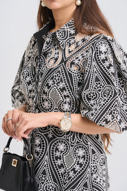 Woman wearing a black and white patterned blouse with a watch on a plain background
