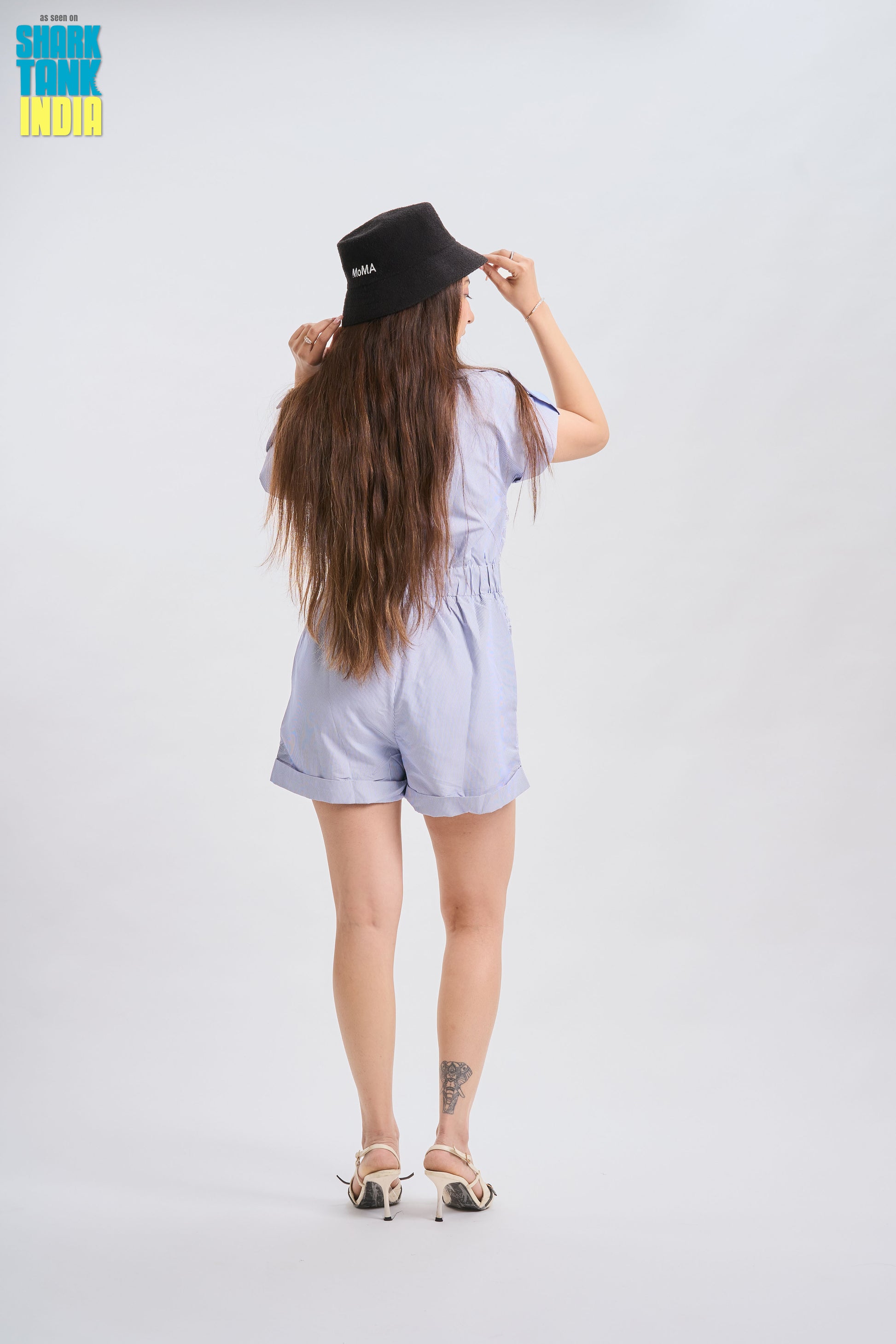 Woman wearing a light blue romper and black hat on a white background