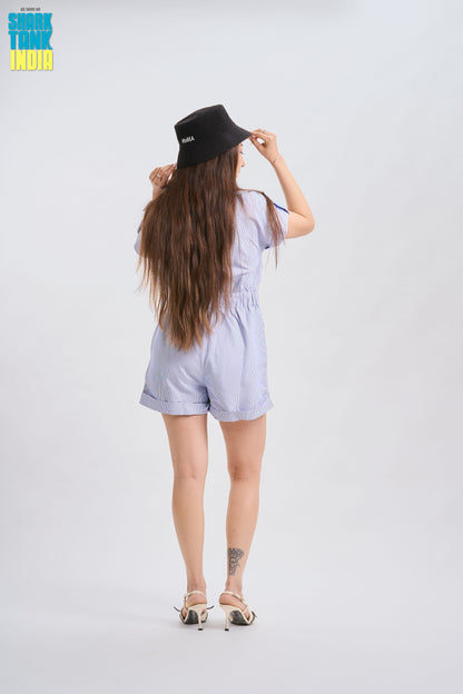 Woman wearing a light blue romper and black hat on a white background