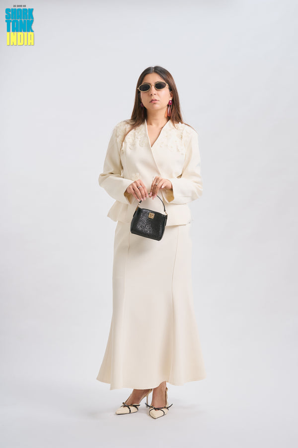 Woman in a cream suit holding a black handbag against a white background