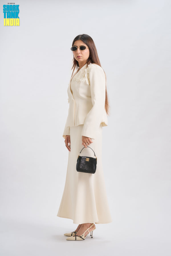 Woman in a white suit holding a black handbag on a white background