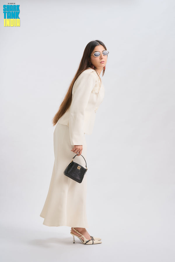 Woman in a white outfit holding a black handbag on a white background