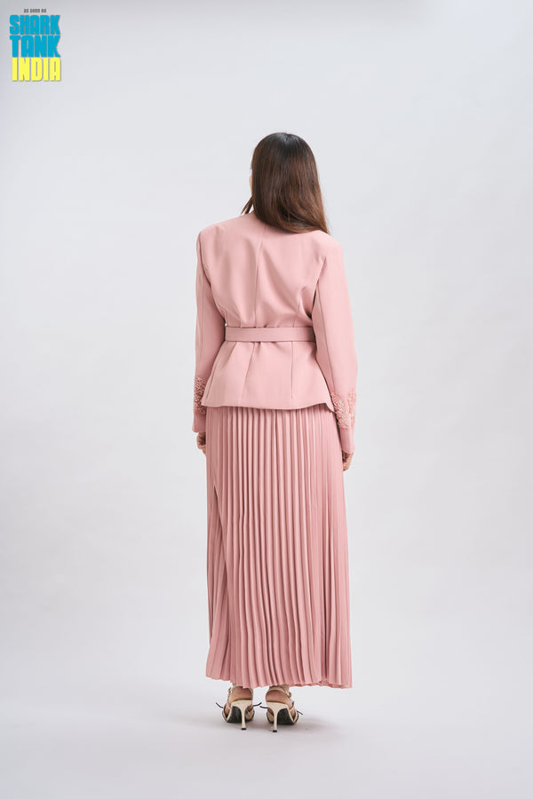 Woman wearing a pink outfit with a jacket and pleated skirt on a white background