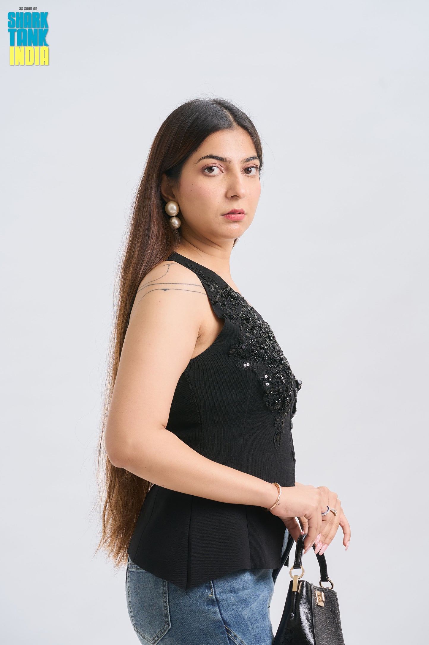 Woman wearing a black sleeveless top with bead details on a white background