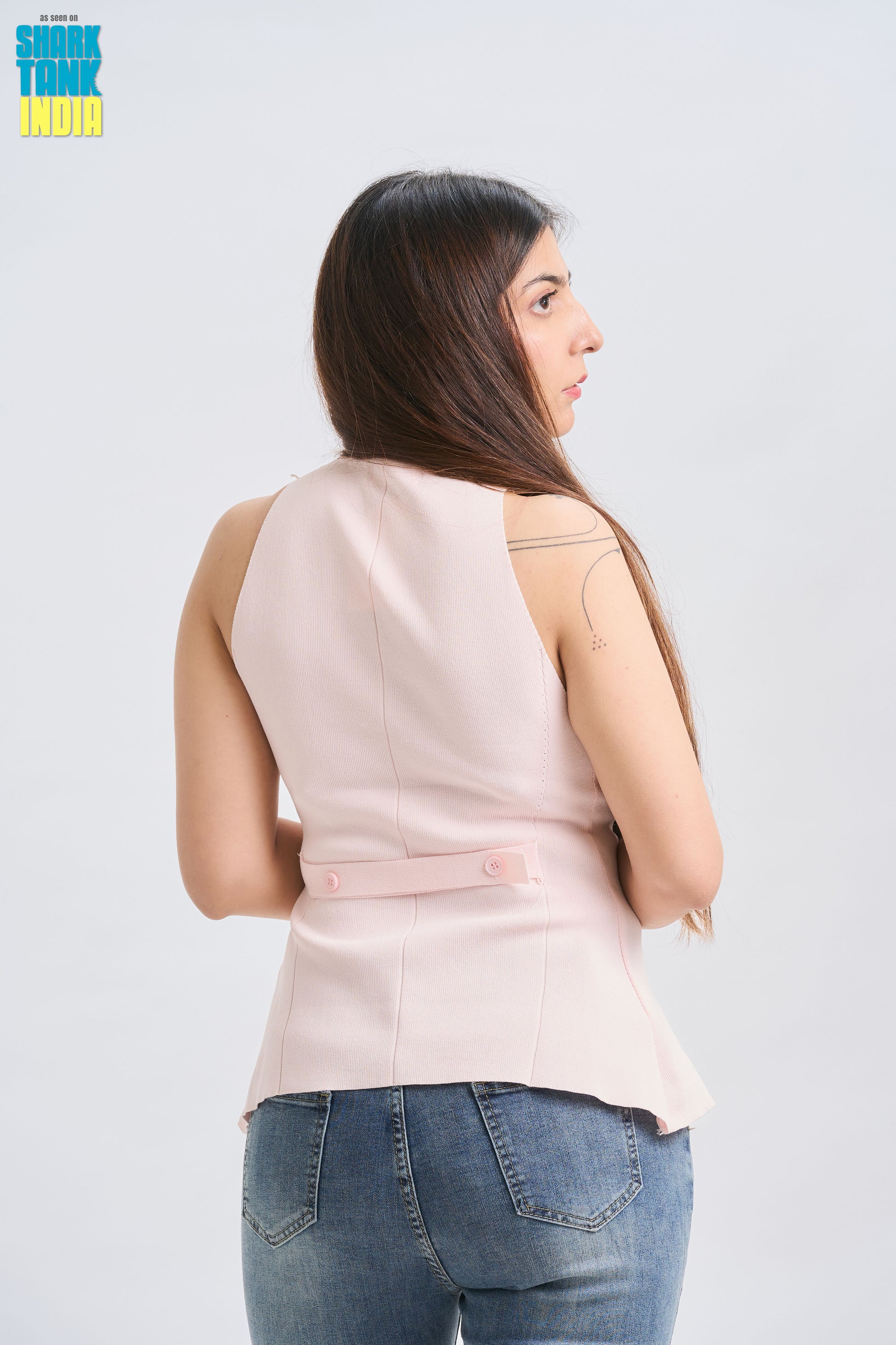 Woman wearing a light pink sleeveless top and blue jeans on a white background