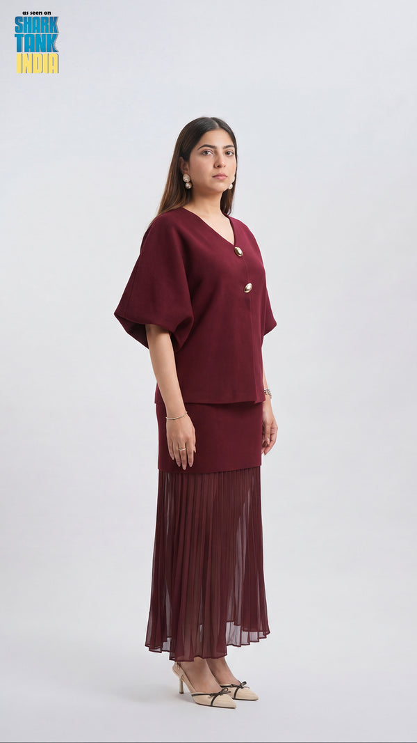 Woman wearing a burgundy outfit with a top and pleated skirt on a white background