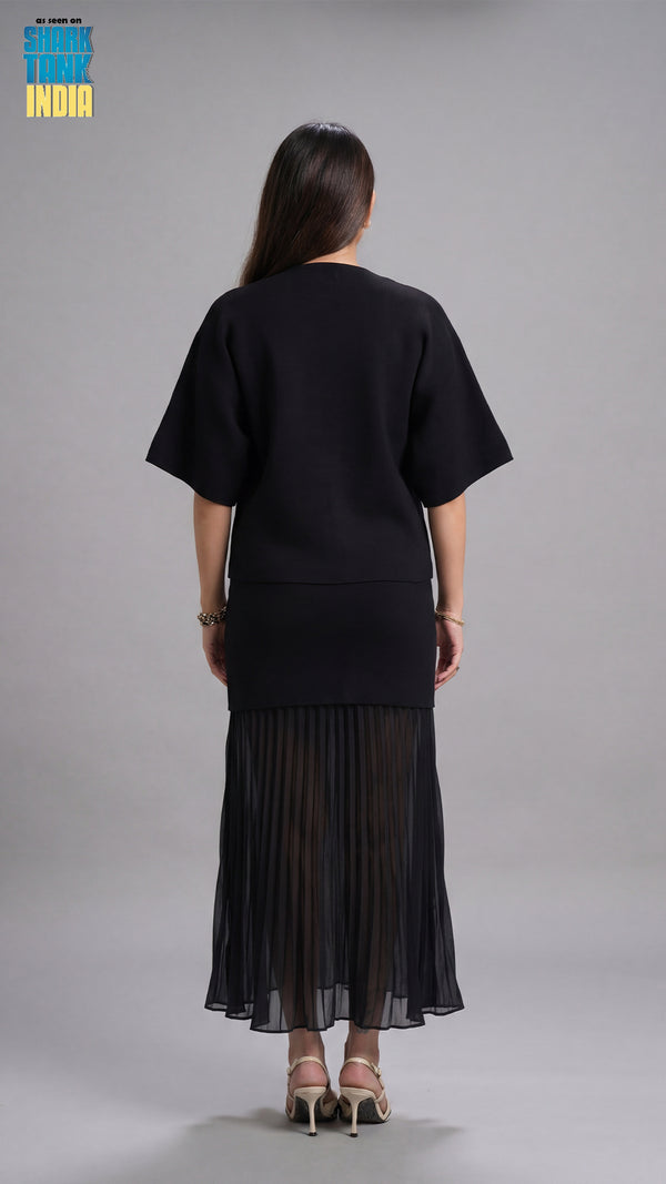 Person wearing a black outfit with a pleated skirt on a gray background